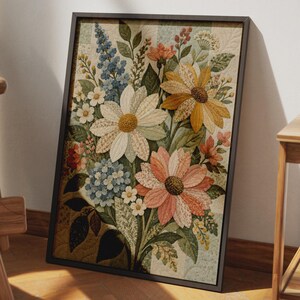 May include: A framed wall art piece featuring a quilted fabric collage of various flowers including large white and orange daisies, blue delphiniums, and small white blossoms. The background consists of a light-coloured, quilted patchwork pattern.