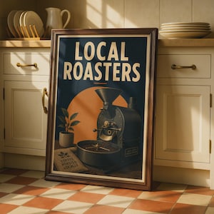 May include: A framed wall art print featuring the text LOCAL ROASTERS in bold white letters. The illustration depicts a dark grey industrial coffee roaster, a small potted plant, and a burlap sack labeled COFFEE ROASTED LOCALLY against an orange sun.