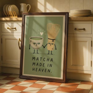 May include: A framed wall art print featuring a cartoon illustration of a matcha bowl and a bamboo whisk holding hands on a sage green background. The text "MATCHA MADE IN HEAVEN." is printed in black below the characters with a small white heart.