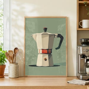 Könnte beinhalten: Gerahmter Druck einer beigefarbenen Kaffeemaschine mit schwarzem Griff und rotem Band. Der Hintergrund ist ein gedämpftes Grün, und der Rahmen ist helles Holz. Der Druck wird auf einer Holz-Arbeitsplatte ausgestellt, was eine Küchen-Dekoration darstellt.