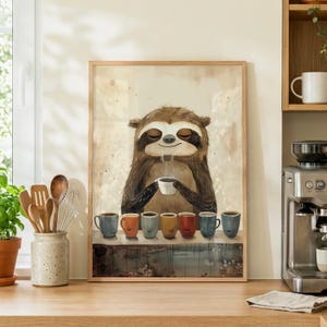 May include: A framed wall art print featuring a brown sloth with closed eyes holding a small white cup. Below the sloth, a row of seven colourful mugs in shades of blue, orange, yellow, and red sits on a dark surface against a light background.