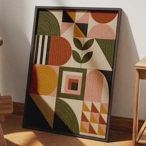 Op de afbeelding: Een ingelijst textielkunstwerk met een geometrisch patchworkontwerp. De compositie bevat doorgestikte vormen in olijfgroen, terracotta, mosterdgeel, roze en zwart, gerangschikt in vierkanten, driehoeken en halve cirkels met een centraal bladmotief.