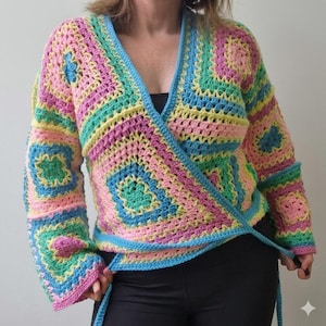 Könnte beinhalten: Ein farbenfroher, handgehäkelter Wickelpullover in Pastelltönen von Rosa, Blau, Gelb und Grün. Der Pullover hat ein quadratisches Muster und einen Wickelstil mit Bindebändern. Die Ärmel sind lang und der Ausschnitt ist V-förmig.