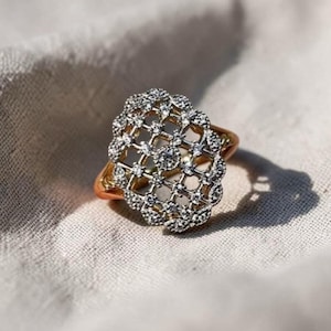 Può includere: Un anello in oro caratterizzato da una parte superiore di forma ovale con un intricato design a reticolo traforato. La superficie del reticolo è incastonata con numerose piccole pietre chiare e scintillanti che coprono l'intera parte superiore.