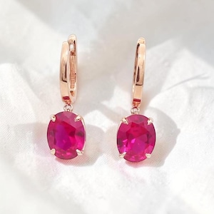 Puede incluir: Un par de pendientes de aro en oro rosa con piedras preciosas ovaladas de color rosa fucsia vibrante facetadas suspendidas de cada aro. Las piedras están aseguradas por cuatro pequeñas garras y el metal tiene un acabado pulido.