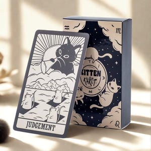Pode incluir: Um baralho de cartas de Tarot de Gatinho com uma ilustração em preto e branco de um gato. A carta diz "Julgamento" na parte inferior. A caixa azul marinho tem ilustrações de gatos brancos e as palavras "Kitten Tarot".
