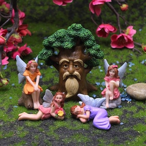 Puede incluir: Una escena de jardín de hadas en miniatura con un árbol con una cara y cuatro hadas. Dos hadas están sentadas, una está acostada y otra sostiene flores. Las hadas visten vestidos en tonos naranja, rosa y morado.