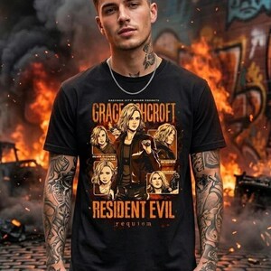 May include: Black t-shirt featuring a graphic of Grace Hcrof, from Resident Evil: Requiem. The design includes portraits and text. The background shows flames and graffiti. The shirt is worn by a person with tattoos and a silver chain.