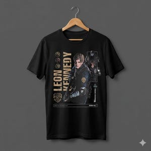 May include: Black t-shirt featuring a graphic of Leon Kennedy from Resident Evil 2. The design includes the text "LEON KENNEDY" in gold, along with images of the character and other game elements. The shirt is hanging on a wooden hanger.