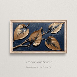 May include: A framed artwork featuring four gold-colored leaves with dark veins against a dark blue background. The leaves are attached to a brown branch. The frame is a light brown color. The artwork is labeled "Lemonicious Studio."