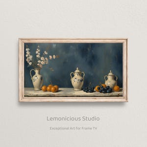 Pode incluir: Pintura de natureza morta emoldurada com um vaso de flores brancas, duas urnas com tampa e uma seleção de laranjas e uvas. A obra de arte tem uma estética vintage com um fundo azul e uma moldura de madeira clara.