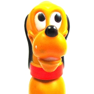 May include: A yellow plastic figurine of Pluto, a cartoon dog from Disney. Pluto is sitting with his tongue sticking out and has a red collar.