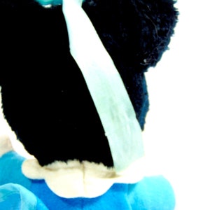 May include: A black and white plush toy with a blue bow. The toy is wearing a blue and white dress.