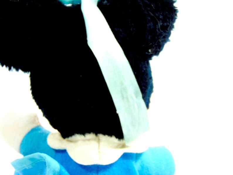 May include: A black and white plush toy with a blue bow. The toy is wearing a blue and white dress.