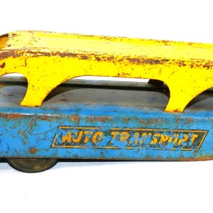 May include: Vintage toy auto transport in blue and yellow. The metal toy has a blue base with the words "AUTO TRANSPORT" and a yellow top. The toy has a distressed, rusty appearance.