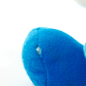 May include: Close-up of a blue plush toy with a small hole in the fabric. The toy is made of soft, fuzzy material.