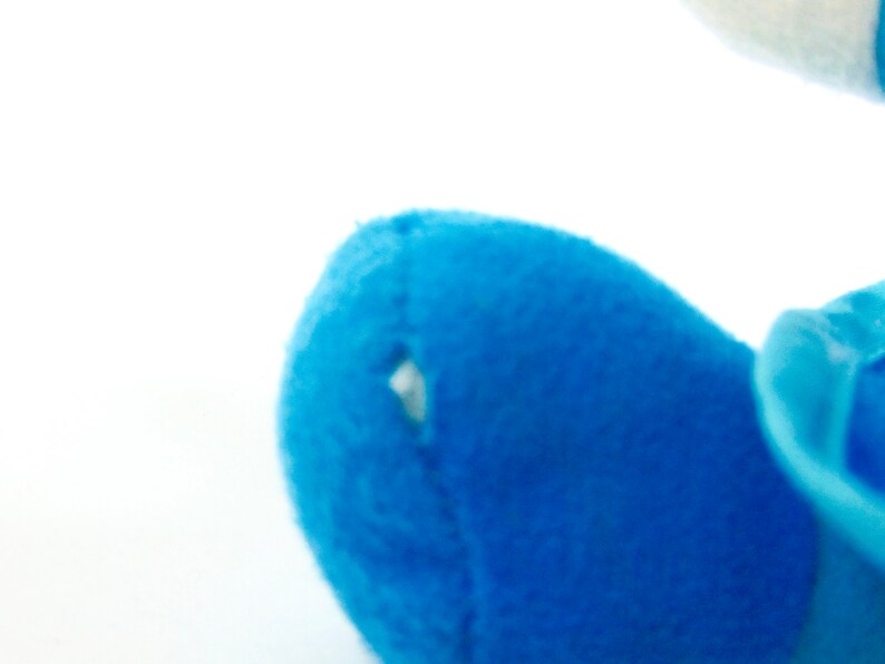 May include: Close-up of a blue plush toy with a small hole in the fabric. The toy is made of soft, fuzzy material.