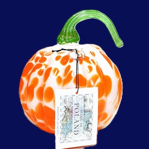 May include: A decorative glass pumpkin with a white base and orange polka dots. The pumpkin has a green stem and a tag that reads "Made in Poland".