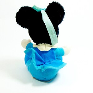 May include: A plush toy of a cartoon mouse wearing a blue dress with a white collar and a blue bow. The mouse has black ears and a black face.