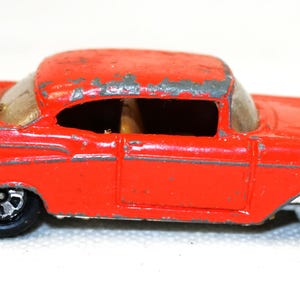 May include: A vintage red toy car with black wheels and silver trim. The classic car has a weathered appearance, with visible paint wear on the roof and body. The toy car is a miniature replica of a classic vehicle.