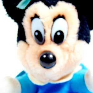 May include: A plush toy of a cartoon character with black ears and a black nose. The toy is wearing a blue and white outfit.