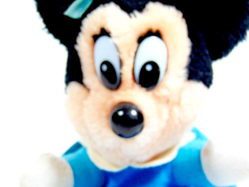 May include: A plush toy of a cartoon character with black ears and a black nose. The toy is wearing a blue and white outfit.