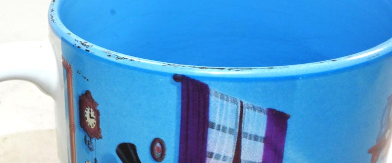 Puede incluir: Una taza de cer&aacute;mica azul con asa blanca. La taza tiene un dise&ntilde;o colorido con un reloj, cortinas y otros detalles.