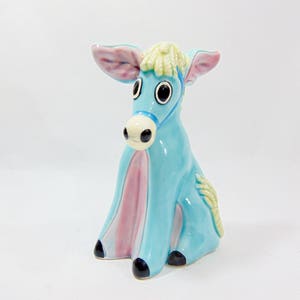 Peut inclure: Une figurine de donkey en céramique bleue avec des accents roses et blancs. L'âne a de grands yeux noirs et une crinière jaune.