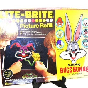 May include: A vintage Lite-Brite Picture Refill box featuring Bugs Bunny and his friends. The box shows children creating a Bugs Bunny picture with colorful pegs. The box includes 12 Lite-Brite pictures and 24 guide sheets.