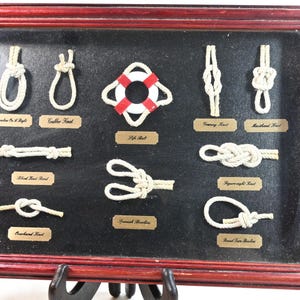 May include: A framed display featuring various nautical rope knots on a black background. The knots are labeled with text including Bowline On A Bight, Grubber Knot, Life Buoy, Granny Knot, Masthead Knot, Reef Knot Bend, Spanish Bowline, Figureeight Knot, Overhand Knot, and Round Turn Bowline.