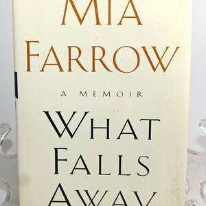 Könnte beinhalten: Ein weißer Buchumschlag mit dem Titel "MIA FARROW A MEMOIR WHAT FALLS AWAY" in orangefarbenem und schwarzem Text.