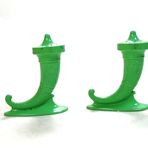 May include: A pair of bright green salt and pepper shakers. Each shaker is shaped like a horn of plenty with a decorative pattern. The top of each shaker has small holes for dispensing salt or pepper.