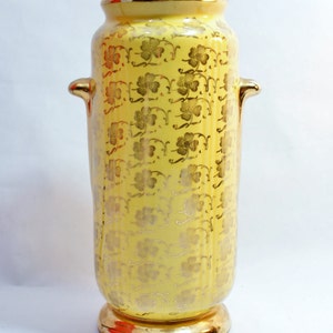 Könnte beinhalten: Eine gelbe Keramikvase mit Blattgold-Verzierungen. Die Vase hat eine zylindrische Form mit zwei Griffen und einem goldenen Rand.
