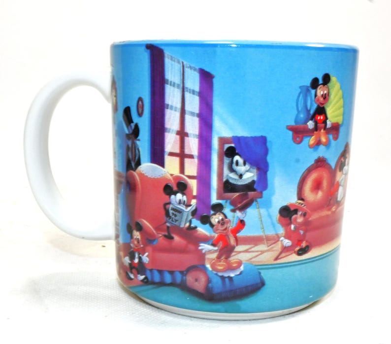 Puede incluir: Una taza de cer&aacute;mica azul con asa blanca presenta una ilustraci&oacute;n de dibujos animados de Mickey Mouse y sus amigos en un ambiente de habitaci&oacute;n. La taza tiene un fondo azul con una ventana, un marco de imagen y un sill&oacute;n rojo.