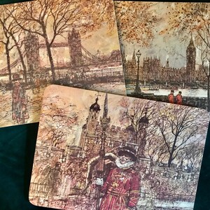 May include: Set of three brown and white illustrated coasters featuring iconic London landmarks: Tower Bridge, Houses of Parliament, and Tower of London. Each coaster depicts a scene with people and trees.