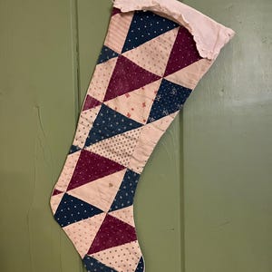 May include: A vintage patchwork Christmas stocking with a white cuff and a geometric pattern of pink, blue, and burgundy triangles.