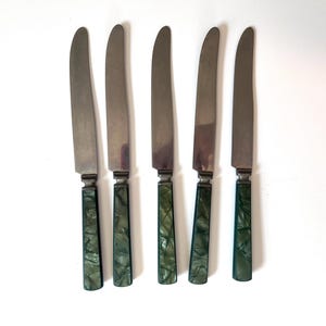 May include: A set of five dinner knives with silver-toned metal blades and handles featuring a green marbled pattern. Each knife has a straight, smooth blade and a rectangular handle with a glossy finish, arranged vertically in a row.