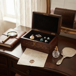 May include: A dark wood jewelry box with an open lid, featuring intricate floral inlay and a metal latch. Inside, the black velvet lining holds several rings and a gold pocket watch. Nearby are a leather-bound journal, a magnifying glass, a glass perfume bottle, a hand mirror, and a handwritten letter with a wax seal.