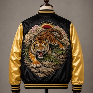 May include: A black satin bomber jacket with gold sleeves and striped black and gold ribbed trim. The back features an embroidered design of a snarling tiger crouching among rocks and green foliage, with pink cherry blossoms and a red sun above.