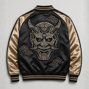 Puede incluir: Chaqueta bomber de satén negro con mangas y ribetes dorados. La espalda presenta una gran máscara Oni dorada bordada con ojos rojos y detalles de nubes. La chaqueta tiene cuello, puños y dobladillo de canalé.