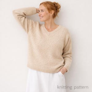 May include: A beige V-neck sweater with a relaxed fit. The sweater is made of a soft, textured knit fabric. The model is wearing a white skirt. The words "knitting pattern" are printed at the bottom of the image.