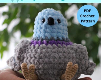 May include: A handmade crochet pigeon toy in shades of blue, gray, and purple. The plush bird has a round body, small wings, and tan feet. The text "Jelly the Pigeon" and "PDF Crochet Pattern" are visible.