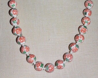 May include: A white porcelain necklace with red and green Chinese characters on each bead.