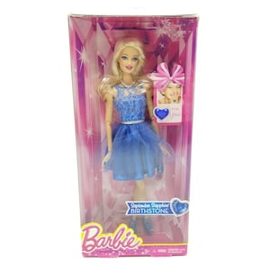 May include: Barbie doll wearing a blue dress with a lace bodice and a tulle skirt. The doll has blonde hair and blue eyes. The box features a pink and white background with a diamond pattern. The text on the box reads "September Sapphire Birthstone".