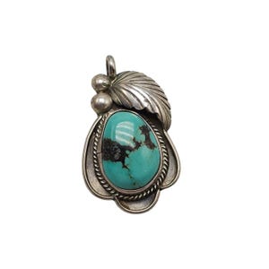 May include: A silver pendant featuring a turquoise stone set within a silver leaf design. The stone is a light blue colour with black veins.