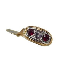 Può includere: Un anello d'oro con una faccia rettangolare, con tre pietre preziose. Due pietre rosse affiancano una pietra centrale trasparente. L'anello ha una fascia dorata e un'incastonatura color argento per le pietre. Su sfondo bianco.