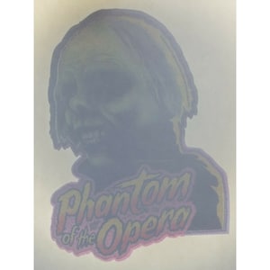 Puede incluir: Un parche de planchado vintage que presenta una figura fantasmal con una sonrisa amenazante y el texto "Phantom of the Opera" en una fuente colorida y estilizada.