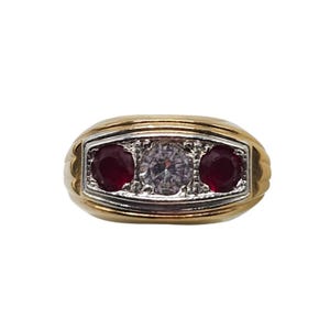 May include: A gold-toned ring with a rectangular face. The face features a central clear stone flanked by two red stones. The ring has a classic, elegant design, suitable for various occasions.