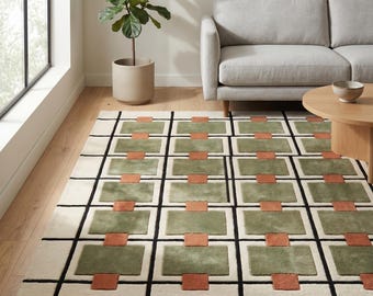 May include: A rectangular rug with a geometric design. The rug has a cream-coloured base with a grid of black lines. Within the grid are rectangular blocks of olive green and terracotta. The rug is in a living room setting, near a sofa and coffee table.