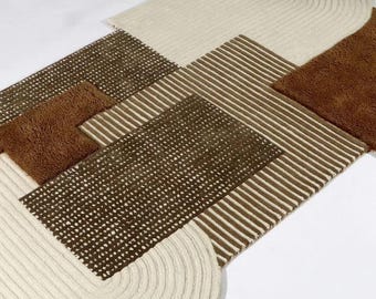 May include: A rectangular area rug featuring a geometric composition of cream, dark brown, and tan sections. The design incorporates textured cream braided borders, a dark brown grid-patterned panel, and a central section with thin brown stripes.